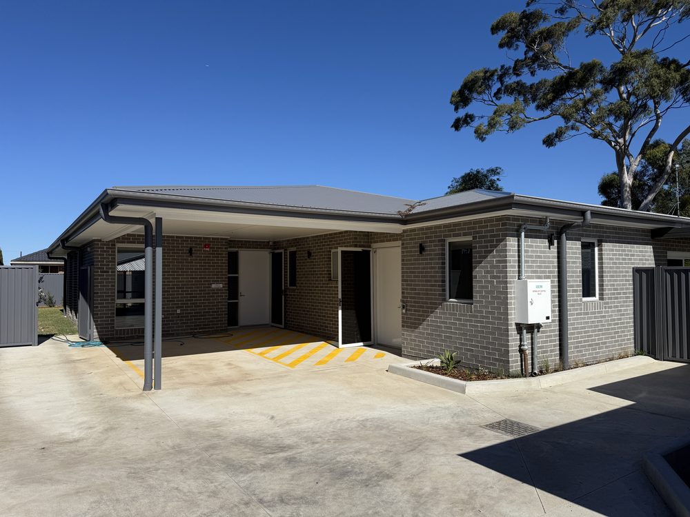 Single storey brick home with a covered accessible entry, level concrete approach and yellow tactile ground indicators